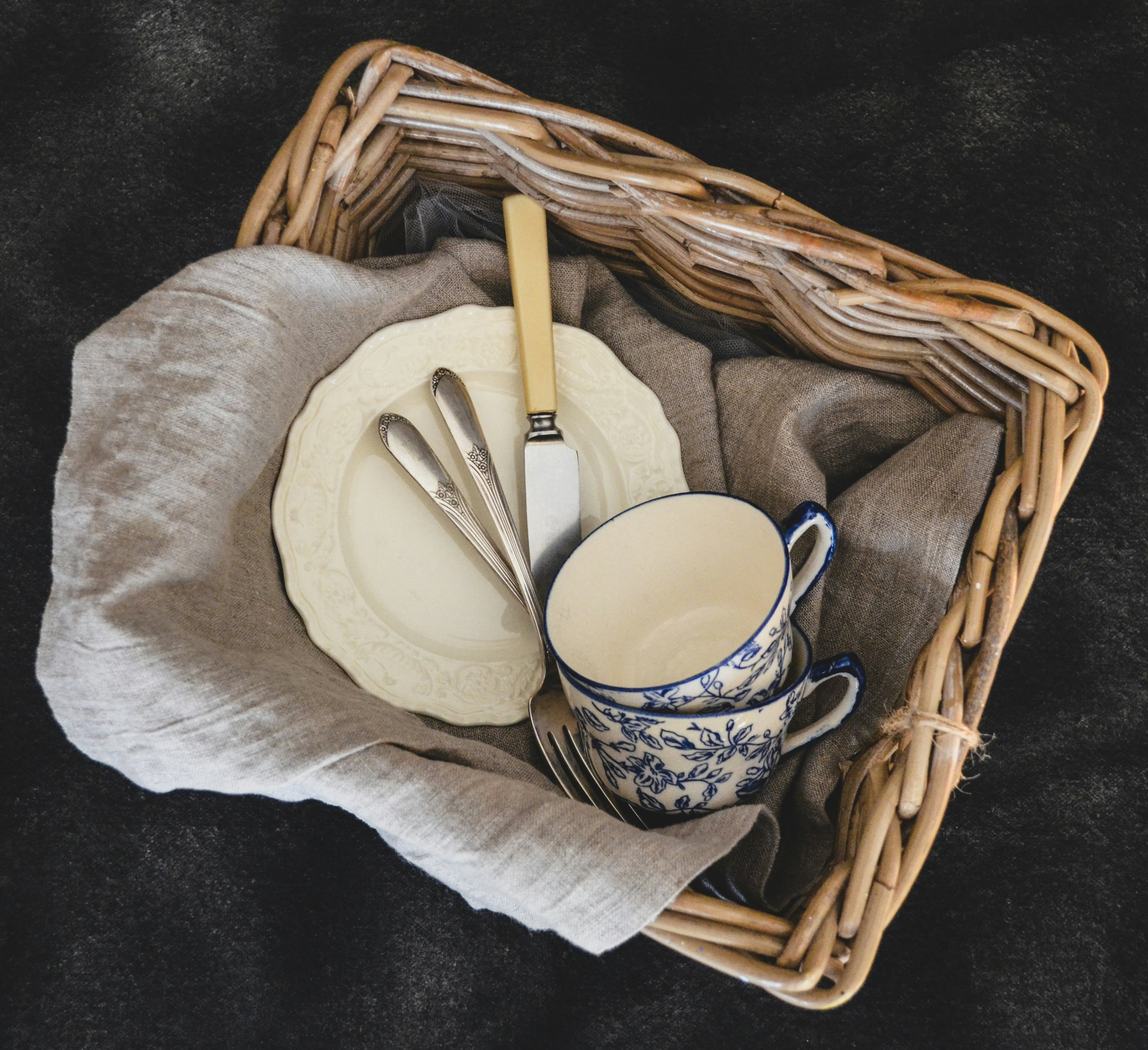 Vaisselle ancienne entourée d'un linge de maison dans un panier de brocante